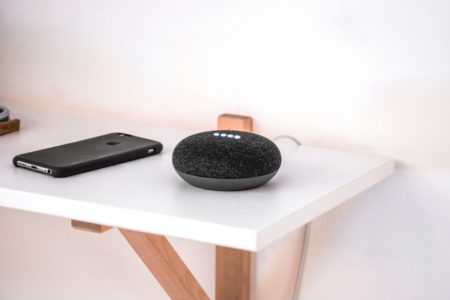 black google home with black smart phone next to it, sitting on white table with white wall